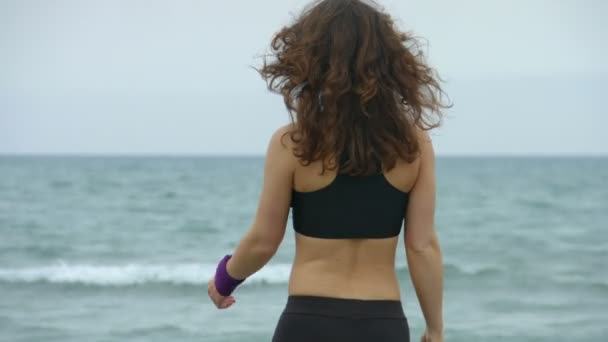 Mujer joven feliz haciendo ejercicio para relajar los músculos después del entrenamiento matutino en el mar — Vídeos de Stock