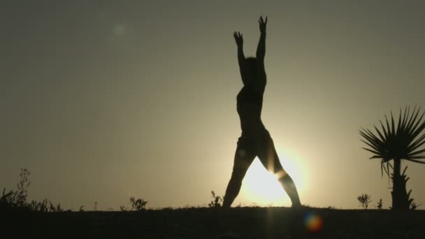 Жіночий силует робить вправи для розтягування тіла, практикуючи йогу в сонячному світлі — стокове відео