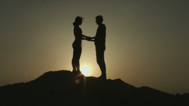 Силуэт влюбленной молодой пары, обнимающей друг друга, целующейся в лучах заката на горе — стоковое видео