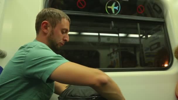 Молодой человек читает новости онлайн, используя приложение, текст на смартфоне в метропоезде — стоковое видео