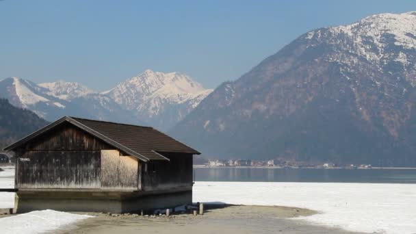 Cabaña de madera abandonada a orillas del lago, panorámica de majestuosa cordillera nevada — Vídeo de stock