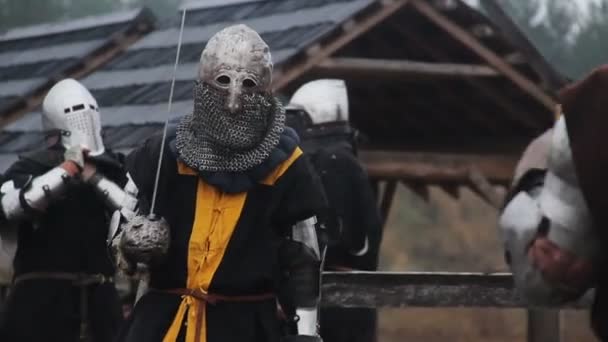 Храбрые воины в средневековых рыцарских доспехах сражаются с мечами под дождем — стоковое видео