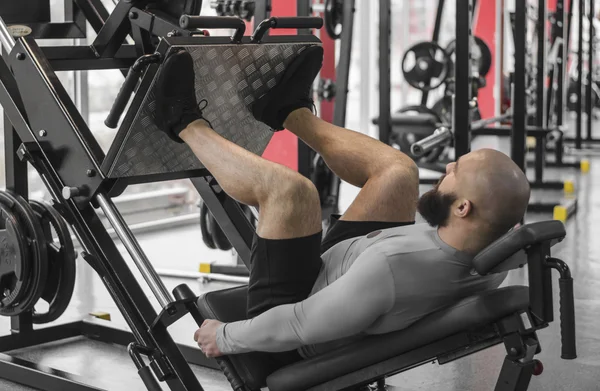 Uomo forte con corpo muscoloso in forma che fa esercizi sulla pressa per le gambe, allenamento — Foto Stock