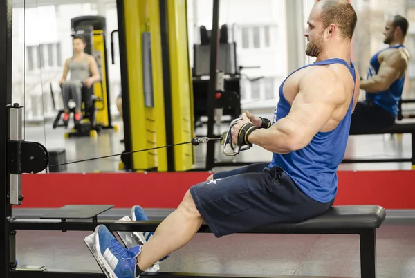 Atleta masculino exitoso haciendo filas de cables sentados, entrenamiento de hombre fuerte en el gimnasio — Foto de Stock