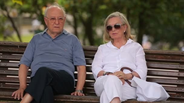 Starší pár, kteří požívají odpočinku na lavičce — Stock video