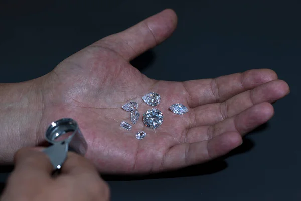 Man jeweller hand holding nice luxury diamond. Grading gem precious stones. Diamond business, industry. Gemology lab examination, expensive goods testing.