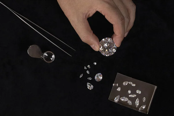 Cut and polished diamonds on black table. Gem stones and hand. Jeweller holding brilliants. Luxury gooda on jewelry store desk.