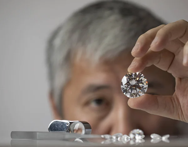 Man jeweller looking at diamond. Big brilliant in hand. Closeup diamond view. Luxury gem handling.