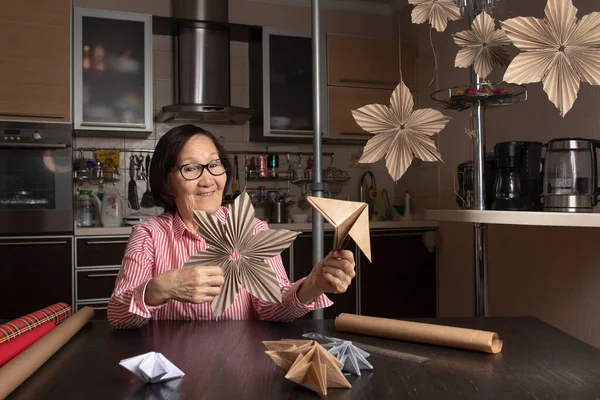 Yaşlı Asyalı kadın blogcu origami atölyesi videosu kaydediyor, seyircilere DIY kağıt dekorasyonu yapmayı öğretiyor. Emeklilik konsepti sıkıcı değil.