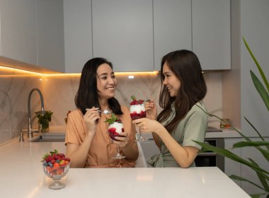 İki güzel genç Asyalı kız kardeş mutfakta taze böğürtlenli yoğurdun tadını çıkarıyorlar. Güzellik ve sağlıklı yaşam tarzı kavramı.