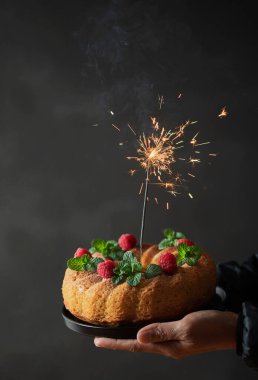 El yapımı kek paketi ahududu ve yanan maytapla süslenmiş. Doğum günü pastası koyu arkaplanda fotokopi alanı ile kapanıyor.