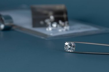 Elindeki elması mücevher araçlarıyla kapat ve arka planda farklı elmasların dağılımını, mavi arka planda ön görünümü.