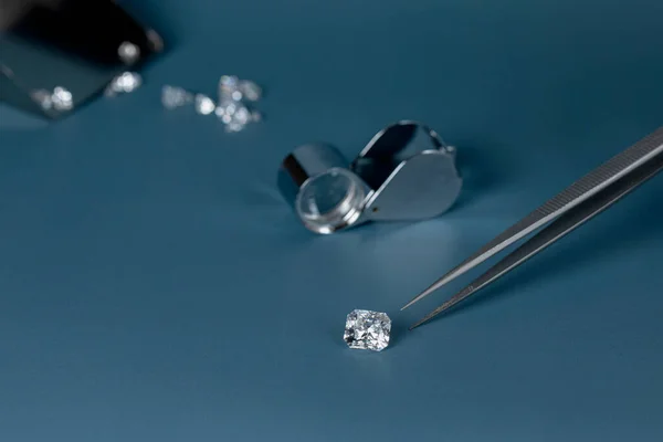 Diamante tagliato in mano da vicino con strumenti di gioielleria e la diffusione di diamanti diversi in background, vista frontale su sfondo blu. — Foto Stock