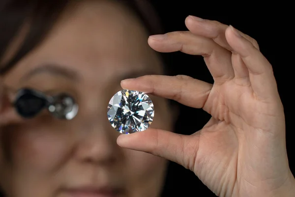 Gros plan de diamant rond en main de femme asiatique évaluant la qualité du diamant à travers la loupe. — Photo