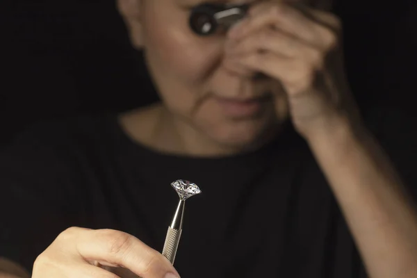 Κοντινό πλάνο του στρογγυλού διαμαντιού στο χέρι της Ασιάτισσας που αξιολογεί την ποιότητα του διαμαντιού μέσα από μεγεθυντικό φακό. — Φωτογραφία Αρχείου