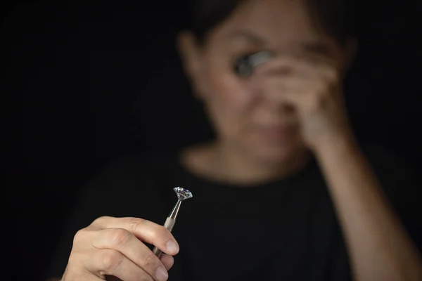 Close up of round cut diamond in hand of asian woman evaluating the quality of diamond through magnifying glass. — Stock Photo, Image