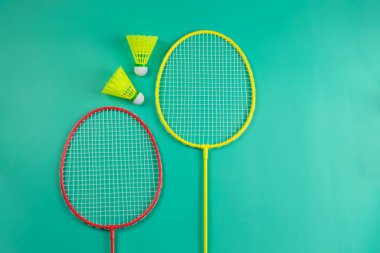 Sarı ve kırmızı badminton raketleri ve parlak yeşil arka plan görünümlü mekik penisleri düz yatıyordu.
