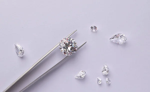 Polished diamonds of various sizes and shapes wit jewelry tools lie at the workplace of an expert examining the quality of stones on light background with copy space.