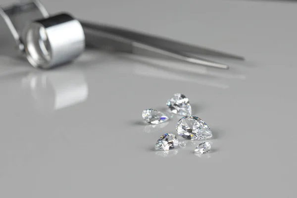 Polished diamonds of various sizes and shapes wit jewelry tools lie at the workplace of an expert examining the quality of stones on light background with copy space. — Stock Photo, Image