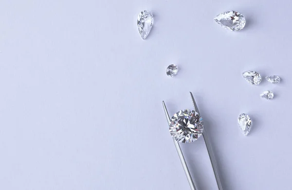 Polished diamonds of various sizes and shapes wit jewelry tools lie at the workplace of an expert examining the quality of stones on light background with copy space.