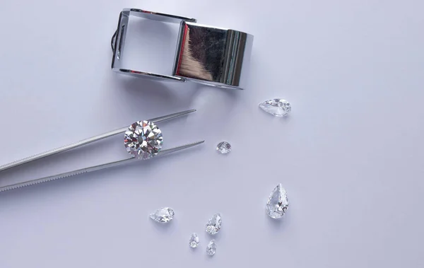 Diamants polis de différentes tailles et formes avec des outils de bijoux se trouvent sur le lieu de travail d'un expert examinant la qualité des pierres sur fond clair avec espace de copie. — Photo