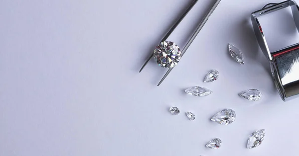 Polished diamonds of various sizes and shapes wit jewelry tools lie at the workplace of an expert examining the quality of stones on light background with copy space.