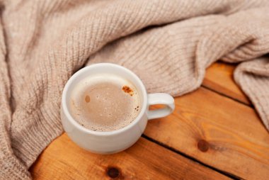 Süt köpüklü kahve, beyaz kupa, örgü bej kazak, ahşap masa, üst manzara, tek renkli rahat kahvaltı fotoğrafı.