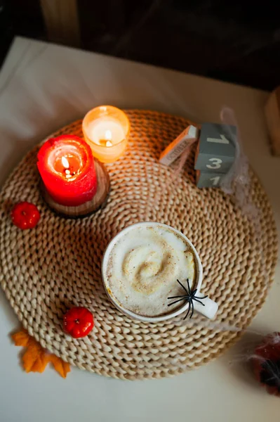 加奶泡沫 香料和蜘蛛的咖啡 在炽热的炉灶上的白色瓷杯中 用锯木柴 蜘蛛网装饰 南瓜和燃烧的蜡烛 朦胧的气氛 万圣节的饮料 节日装饰 — 图库照片