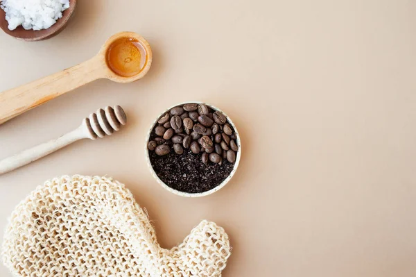 Coffee scrub and coffee beans in gold jar, honey, cosmetic oil and wooden stick for honey against a pastel beige background, home cosmetics, cosmetic layout anti-cellulite products, selective focus