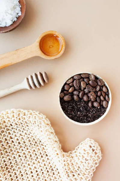 Coffee scrub and coffee beans in gold jar, honey, cosmetic oil and wooden stick for honey against a pastel beige background, home cosmetics, cosmetic layout anti-cellulite products, selective focus