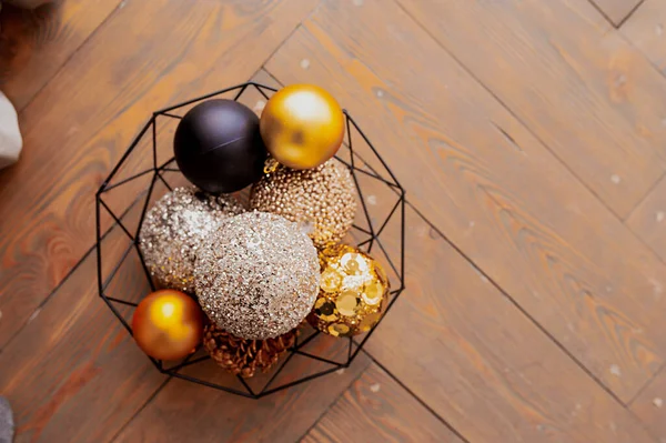 gold, beige and black shiny balls for Christmas decor in a metal black basket on a wooden cover. holiday card, selective focus