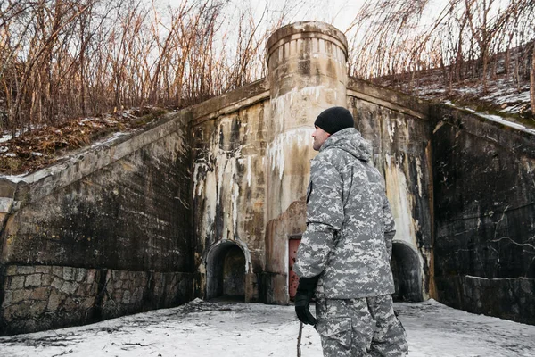 man in military camouflage clothing on background of winter landscape near an old concrete castle. interesting local tourism, selective focus