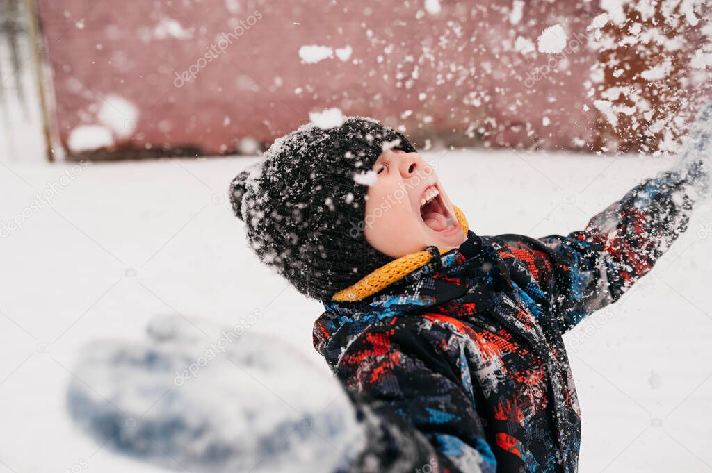 preschool boy throws snow and is very happy about the winter in warm clothes, hat, yellow snood, real life child portrait close-up, selective focus