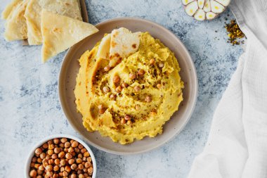 chickpea hummus with olive oil, garlic, spices and roasted grains on kitchen table with bowl of fried chickpeas and traditional tortillas, simple recipes for cooking at home, selective focus