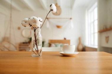 Beyaz porselen bardak ve cam vazoda doğal pamuk buketi dairenin parlak iç kısmında ahşap tezgahta boho tarzında. seçici odak