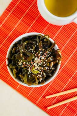 Asyalı konserve deniz yosunu salatası soğan ve susam tohumları kırmızı Asya peçetesi, yemek çubukları ve miso çorbası üzerine beyaz yuvarlak tabakta. dikey üst görünüm, seçici odak