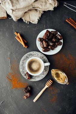 Doğu yemeği. Taze demlenmiş kahve, kurutulmuş hurma, tarçın çubukları, bal dökülmüş kahve ve baharatlar, koyu arkaplanda çuval bezi. Ulusal gıda ve içeceğin renkli görüntüsü. Üst görünüm, seçici odak