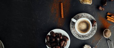 Uzun format afiş, taze kahve, kurutulmuş tarihler, tarçın çubukları, bal, dökülen kahve ve baharatlar, koyu arkaplanda çuval bezi. Ulusal gıda ve içeceğin renkli görüntüsü. Üst görünüm, seçici odak