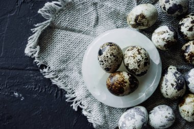 Mermer tabakta küçük benekli bıldırcın yumurtaları ve siyah masanın üzerinde gri çuval bezi. seçici odak