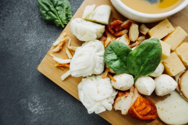 Peynir tabağında taze fesleğen yaprağı. Farklı tipte ev yapımı peynirler. Yemek içeriği. Restoran için peynir menüsü. seçici odak