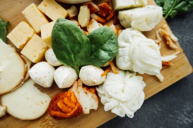 Peynir tabağında taze fesleğen yaprağı. Farklı tipte ev yapımı peynirler. Yemek içeriği. Restoran için peynir menüsü. seçici odak