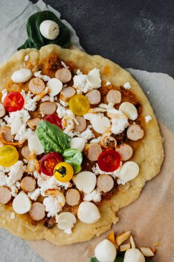 Tavuklu çiğ pizza, domates, mazzarella peyniri ve fesleğen kabartma kağıtlı karanlık bir masada. Sıradan ev yapımı yemekler hakkında bir blog için yemek içeriği. seçici odak