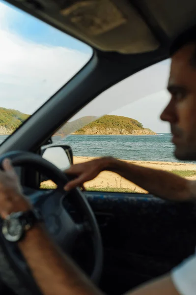 view from open car window of sea, mountain and wild nature and blurred unrecognizable man behind wheel. car trips in summer by sea. real-life moment of summer hitchhiking. selective focus