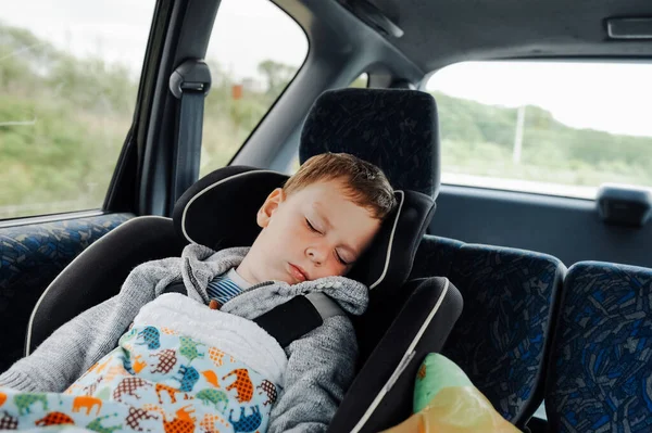 preschool boy sleeps in back seat of car in protective child seat. car trips with children. family local adventures small family . selective focus