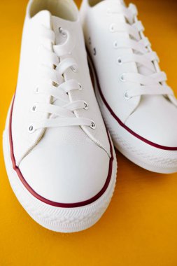 white new clean sneakers with white laces on a rubber sole on a bright yellow background. selective focus clipart