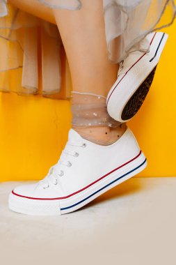 Beyaz, temiz, yeni spor ayakkabılı kadın bacakları şeffaf, parlak gümüş renkli çoraplar ve sarı arka planda gür tül elbiseler. Spor ayakkabıları ve resmi kıyafetlerin birleşimi. seçici odak