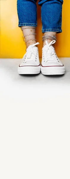 long format banner, women legs in white clean new sneakers, transparent thin socks with silver shiny stars and blue jeans on yellow background. minnelial lifestyle. selective focus