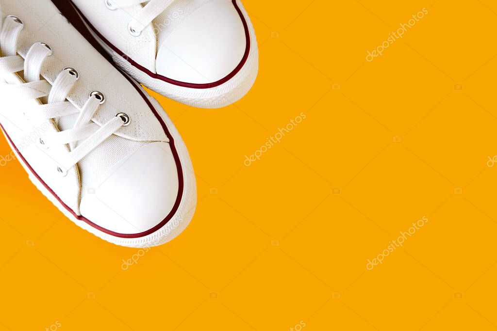 white new clean sneakers with white laces on a rubber sole on a bright yellow background. selective focus