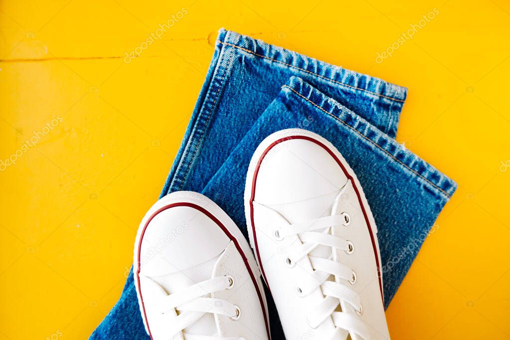 white new clean sneakers with white laces on a rubber sole and blue jeans on a bright yellow background. stylish clothing content. selective focus