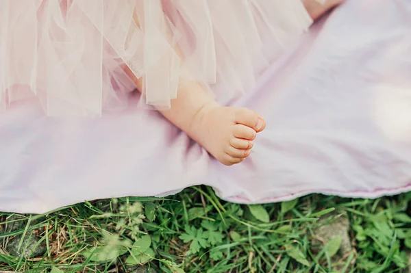 pretty little naked feet of girl on pink plaid in lush pink tulle skirt on green lawn. selective focus